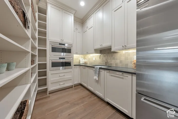 Full-height shelving, light-toned cabinetry, built-in stainless steel appliances, dark countertops, and wood-finish flooring
