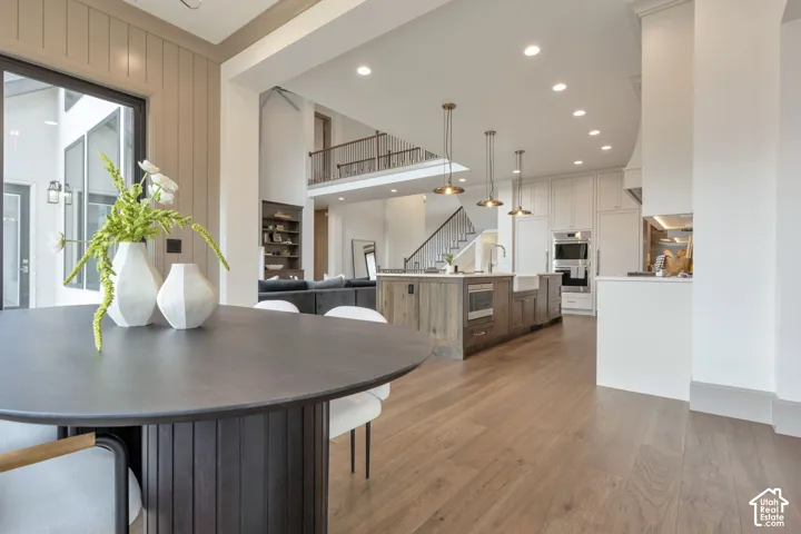 Wood-finish flooring throughout, kitchen with built-in appliances, central island with integrated sink, open-concept design, and a visible second story with railing