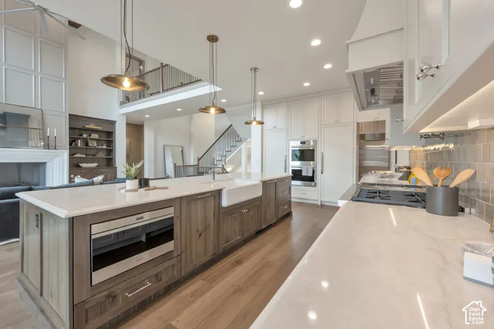 Gourmet kitchen featuring a large island, farm sink, wood-finish flooring, integrated appliances, and a tile backsplash