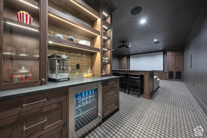 Built-in cabinetry with under-cabinet lighting, integrated beverage refrigerator, large projection screen, and patterned carpeting