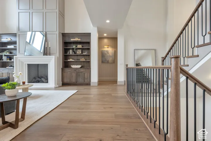 Hardwood flooring, white fireplace, built-in shelving, paneled accent wall, and an open stairwell with black iron balusters