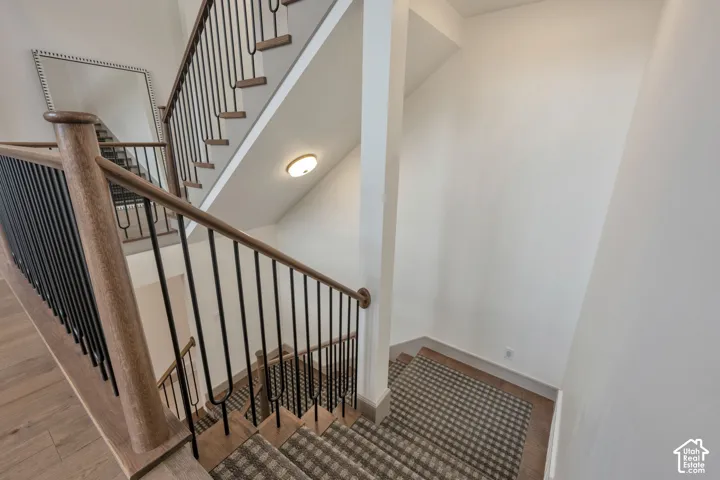 Staircase with wood-finish handrails, black metal balusters, and a carpeted runner