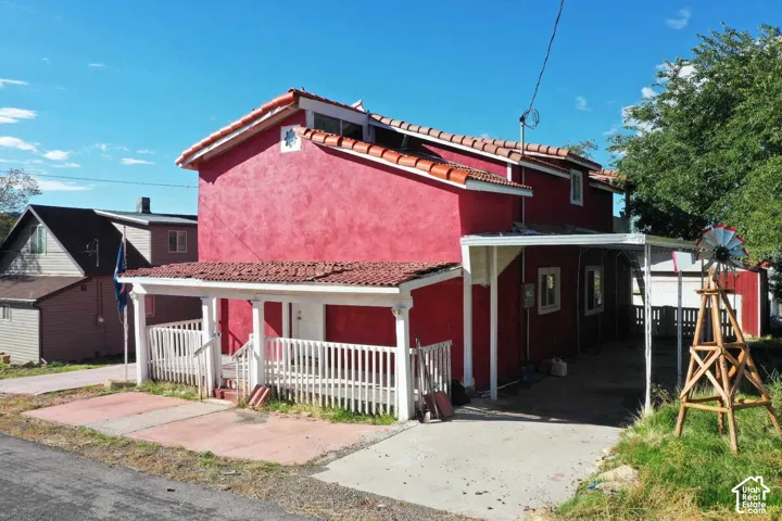 Red stucco exterior with a tiled roof, covered front porch with white railing, covered carport, and a decorative windmill
