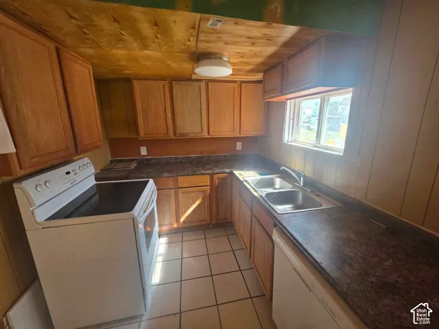 Kitchen featuring wood cabinetry, white tile flooring, a dual basin sink, and an electric range