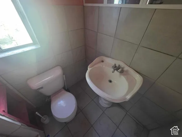 Pedestal sink, wall-mounted faucet, toilet, and tiled walls with a window