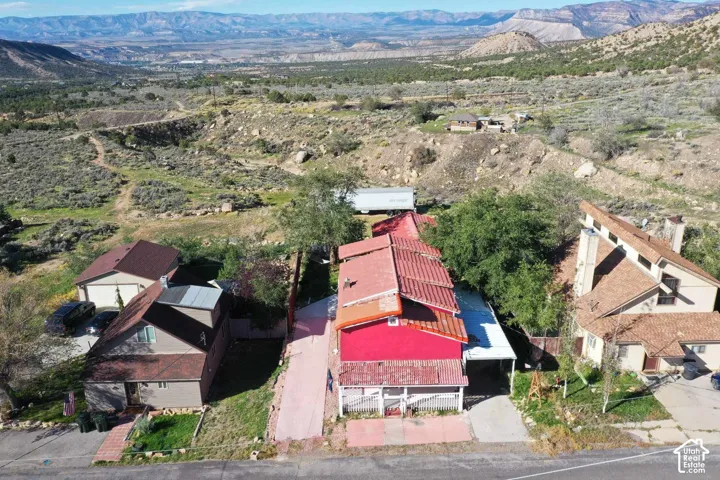 Property situated on a sloped landscape with a red-roofed residence and a tan-sided residence, both featuring brown shingle roofing