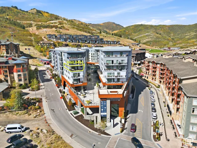 Multistory building featuring modern architecture, multiple balconies, a ground-level patio space, and surrounding mountainous terrain