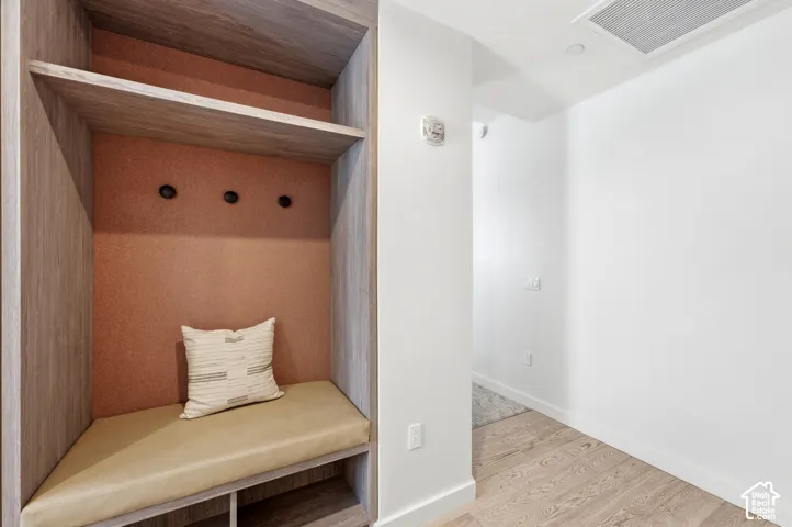 Built-in bench with upholstered seating, integrated shelving, three wall-mounted hooks, and wood-finish flooring