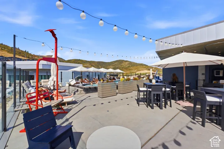 Rooftop lounge area featuring a pool, string lighting, multiple outdoor seating areas, and a glass safety barrier