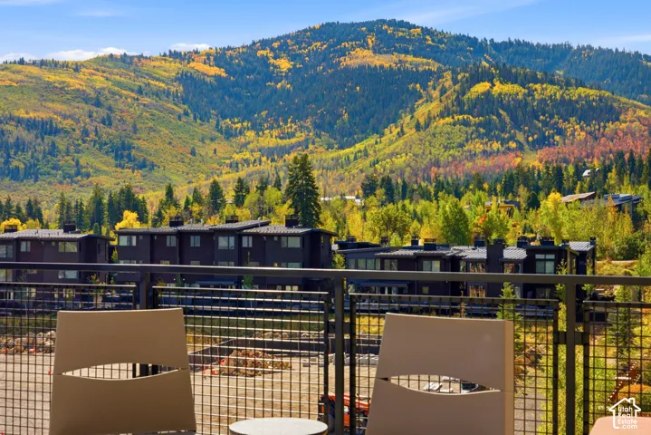 Metal railing, mountain backdrop, distant residences, natural landscaping, clear sky