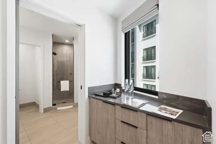 Recessed shower with frameless glass enclosure, wood-finish flooring, built-in cabinetry, and a large window with roller shades