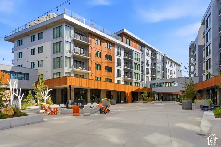 Modern building exterior with multiple balconies, rooftop terrace, and ground-level retail spaces