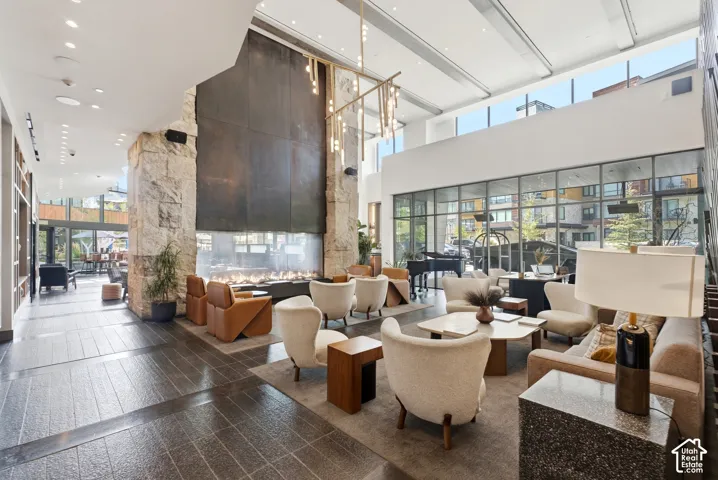Spacious common area featuring a grand fireplace with stone surround, high ceilings, expansive glass paneling, and large format floor tiles