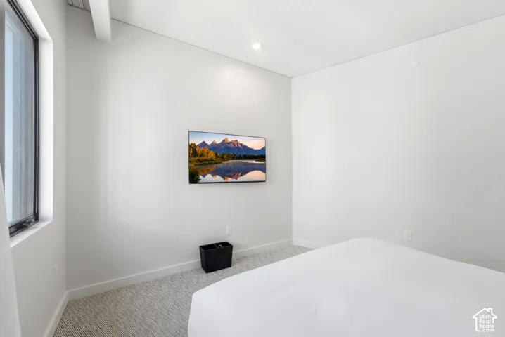 Recessed ceiling lighting, wall-mounted television, wood-finish flooring, and a large window with vertical blinds