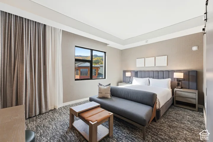 Recessed ceiling with integrated lighting, window with mountain scenery, upholstered headboard, patterned wallcovering, and abstract-patterned carpeting