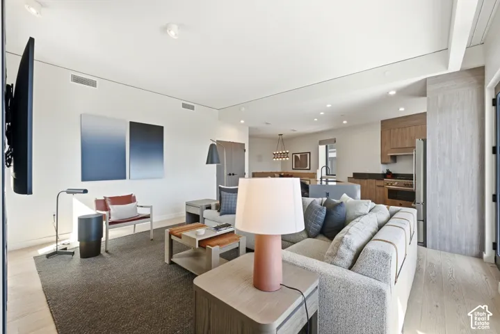 Open-concept living area with light wood-finish flooring, recessed lighting, and a kitchen featuring wood cabinetry, stainless steel appliances, and a dark countertop