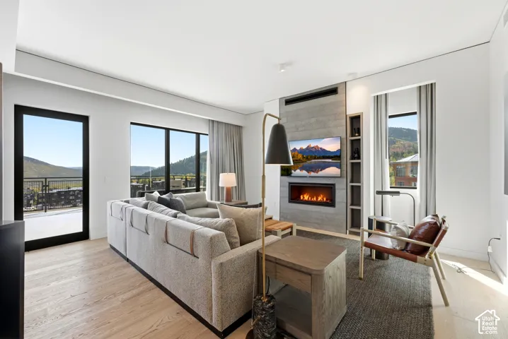 Wide plank wood-finish flooring, full-height windows, a built-in fireplace, and integrated shelving flank the accent wall