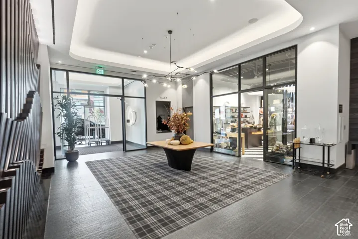 Glass storefronts, recessed lighting, and a plaid area rug complement the dark tile flooring and sculptural wall paneling