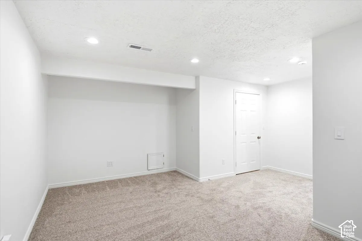 Recessed ceiling lighting, textured ceiling finish, neutral tone carpeting, white painted walls, and white paneled door
