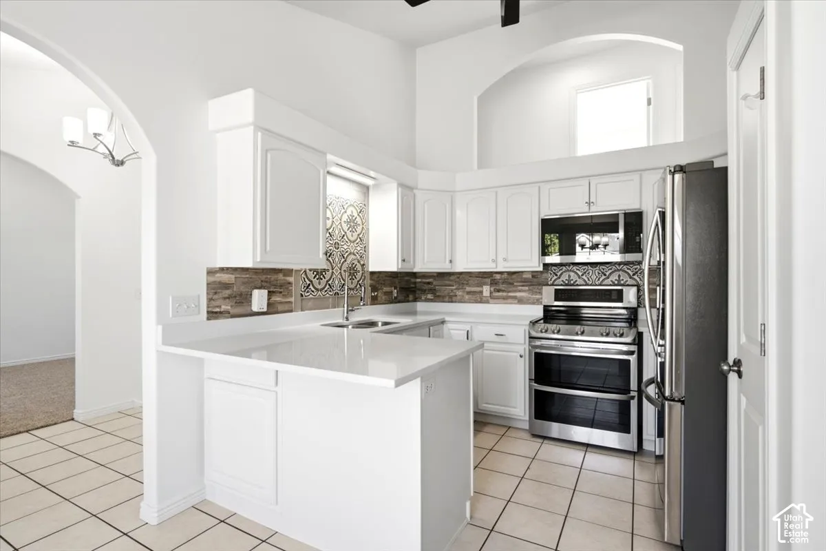 White cabinetry, stainless steel appliances, tile flooring, stone countertops, and decorative tile backsplash