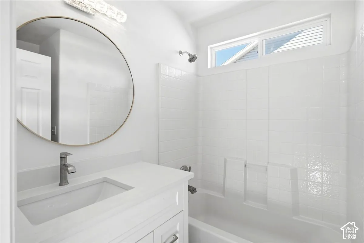 Master bathroom featuring a circular framed mirror with integrated lighting, white subway tile surround, floating vanity with rectangular vessel sink, matte black faucet, and a separate shower enclosure with glass panel and transom window for natural ligh