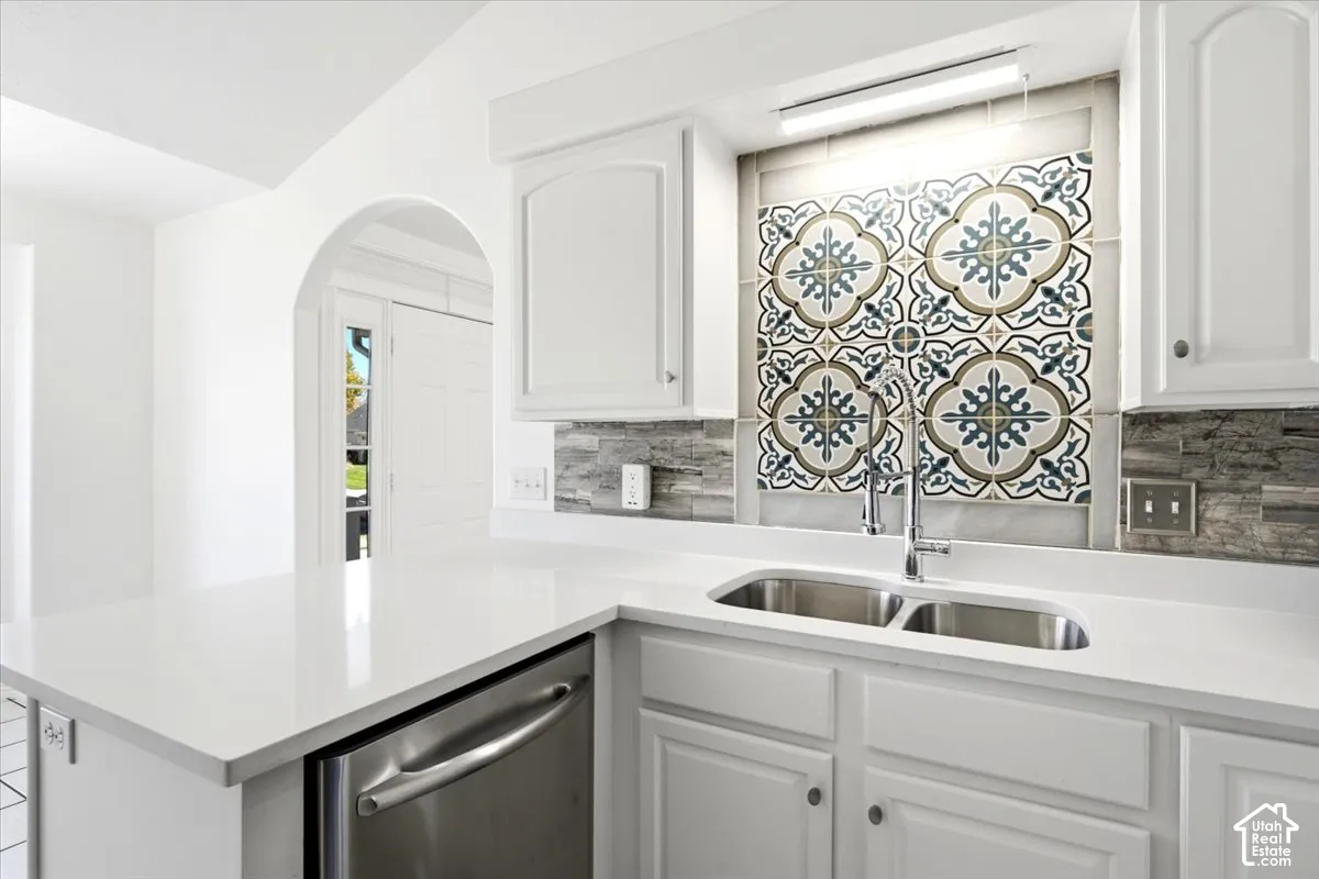 White cabinetry, white countertop, stainless steel double basin sink, decorative tile backsplash, and an arched entryway