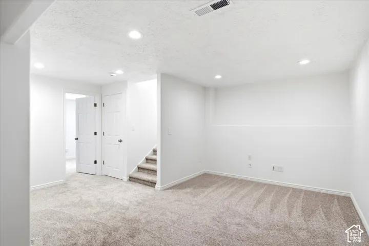 Neutral-toned carpet flooring, recessed ceiling lighting, textured white walls, white paneled doors with dark hardware, and carpeted stairs
