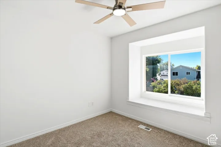 Bedroom #3 - Neutral wall color, carpeted flooring, large deep window seat with storage, and a ceiling fan with integrated lighting