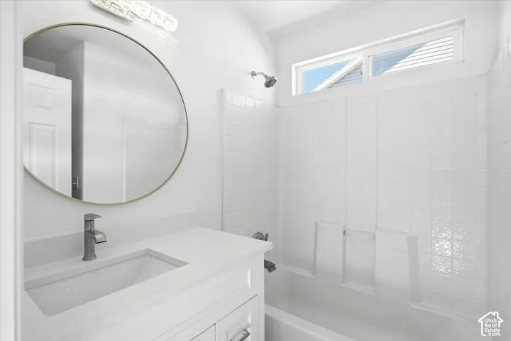 Master bathroom featuring a circular framed mirror with integrated lighting, white subway tile surround, floating vanity with rectangular vessel sink, matte black faucet, and a separate shower enclosure with glass panel and transom window for natural ligh
