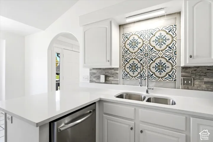 White cabinetry, white countertop, stainless steel double basin sink, decorative tile backsplash, and an arched entryway
