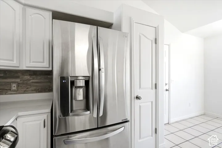 Stainless steel French door refrigerator with ice and water dispenser, white cabinetry, dark stone-look backsplash, light countertop, and tile flooring