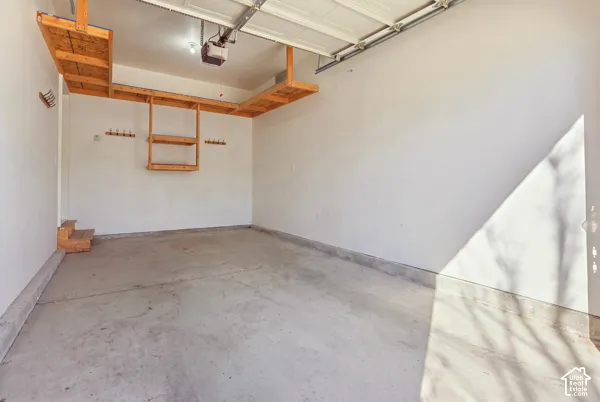 Garage space featuring finished walls, concrete flooring, overhead wood shelving, and wall-mounted storage hooks