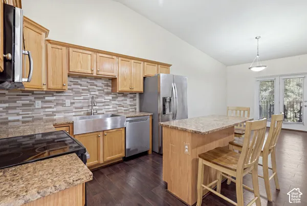 Kitchen featuring natural wood cabinetry, stone-finish countertops, stainless steel farmhouse sink, stacked-tile backsplash, and wood-finish flooring