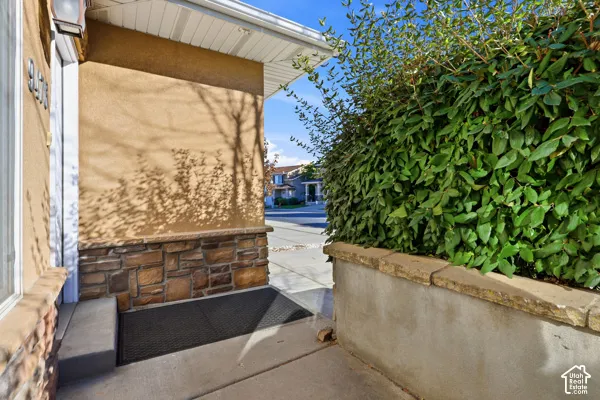 Exterior entryway featuring textured stucco siding, decorative stone veneer, a concrete walkway, and a masonry retaining wall