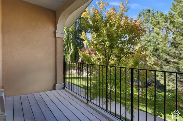 Covered balcony with smooth stucco finish, arched architectural detail, wood-plank flooring, and black metal railing