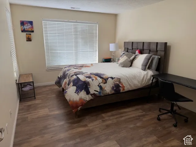 Spacious bedroom featuring a wood-finish plank floor, large window with plantation shutters providing natural light, and a padded upholstered headboard