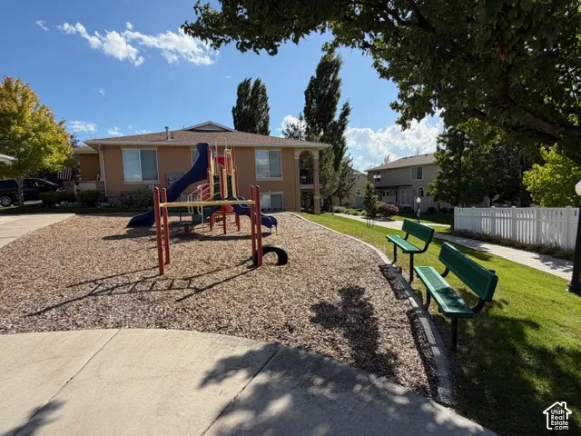 Recreational area featuring a playground structure on wood chips, a manicured lawn, and two green park benches