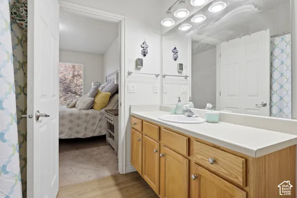 Bathroom vanity featuring a light-tone wood cabinet, solid-surface countertop with an integrated oval sink, full-width mirror, and multi-bulb vanity lighting