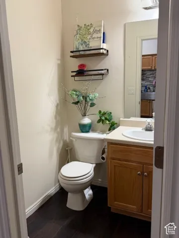 Compact powder room featuring a white ceramic toilet, wood-finish vanity with cabinet storage, and dark tile flooring