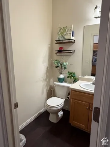 Powder room featuring dark wood-finish flooring, a neutral color palette, a vanity with a light-colored countertop, and a wall-mounted mirror