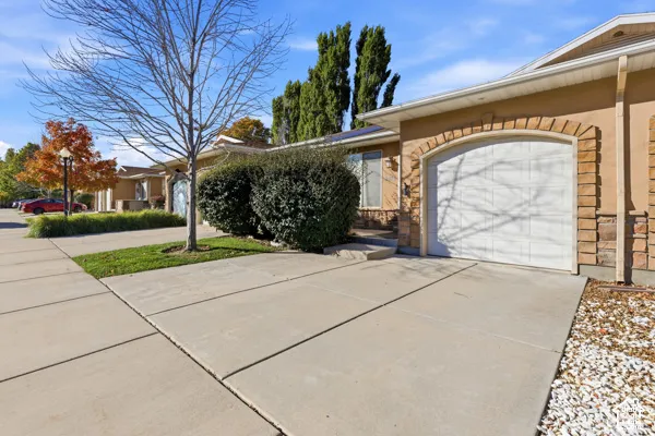 Single-story exterior featuring a concrete driveway, attached garage with an arched stone surround, stucco facade, and landscaped front lawn