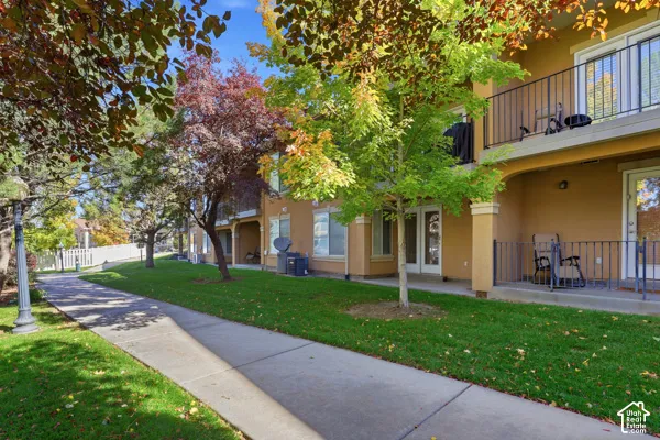 Stucco exterior building featuring private balconies, metal railings, concrete walkways, and manicured landscaping