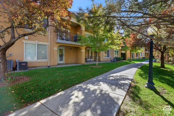 Stucco exterior featuring second-level balconies with decorative metal railings, concrete walkway, and manicured landscaping