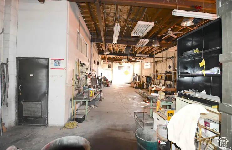 Exposed wood beam ceiling, concrete flooring, fluorescent lighting, overhead fan, and an interior door