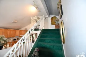 Vaulted ceiling with track lighting, green carpeted staircase, white railing with decorative balusters, and wood-finish cabinetry