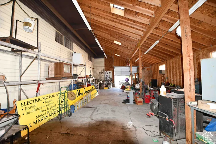 Exposed wood beam ceiling, skylights, concrete flooring, fluorescent lighting, and a roll-up door
