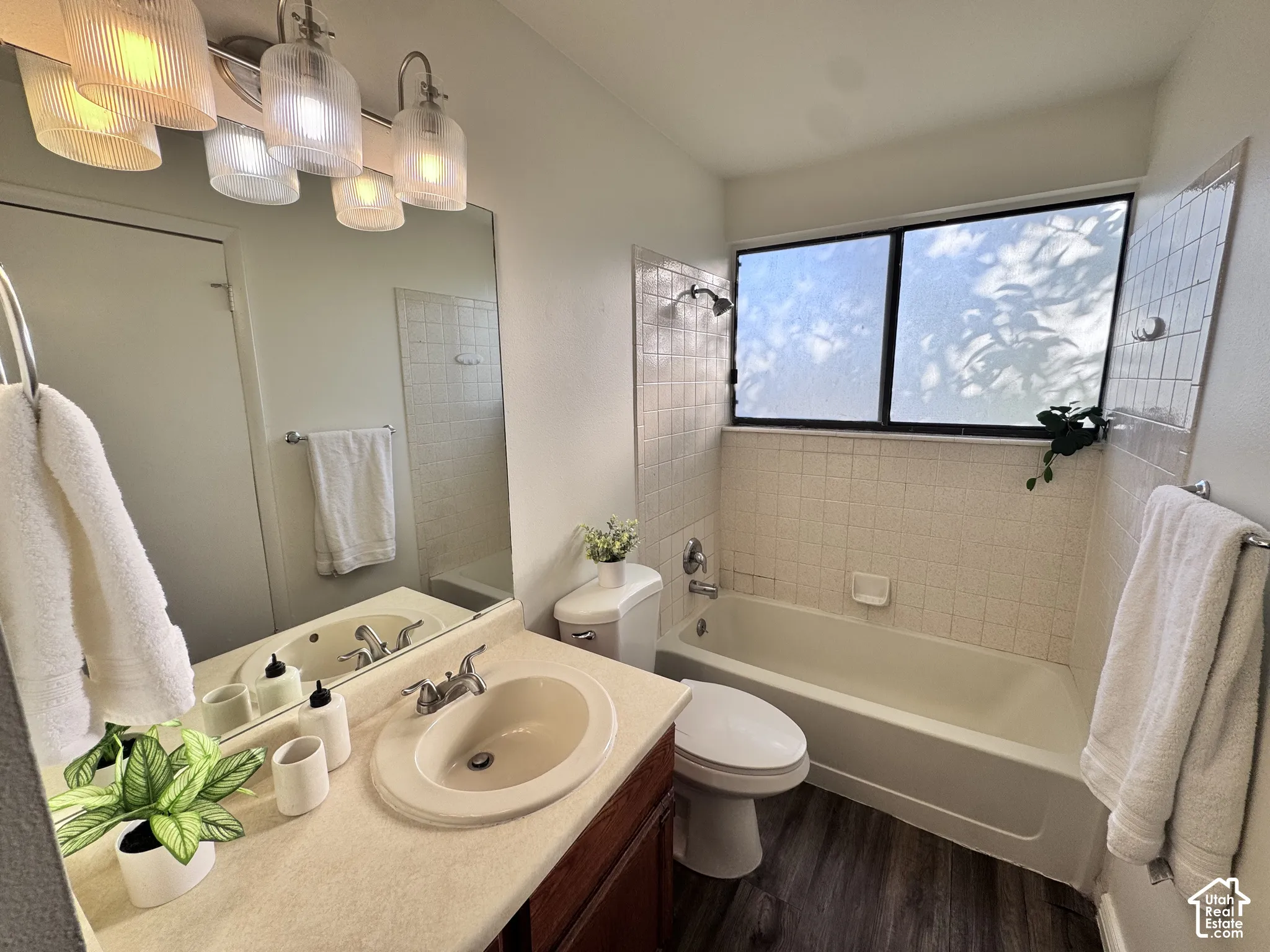 Bathroom featuring a vanity with an integrated sink, a rectangular mirror, a bathtub with a tiled surround, a window, and wood-finish flooring
