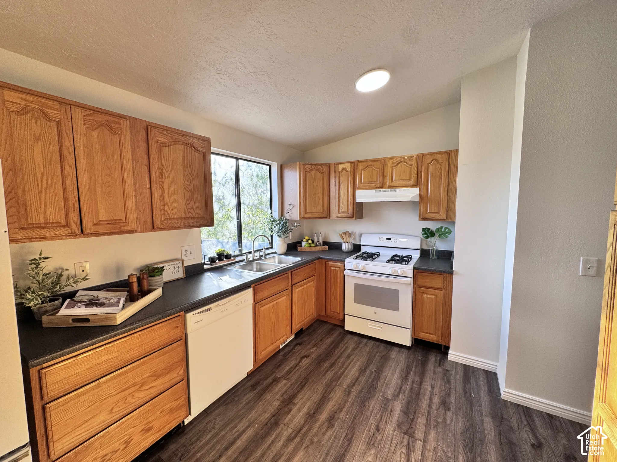 Wood-finish flooring, wood cabinetry, built-in dishwasher, white range with hood, and a dual basin sink