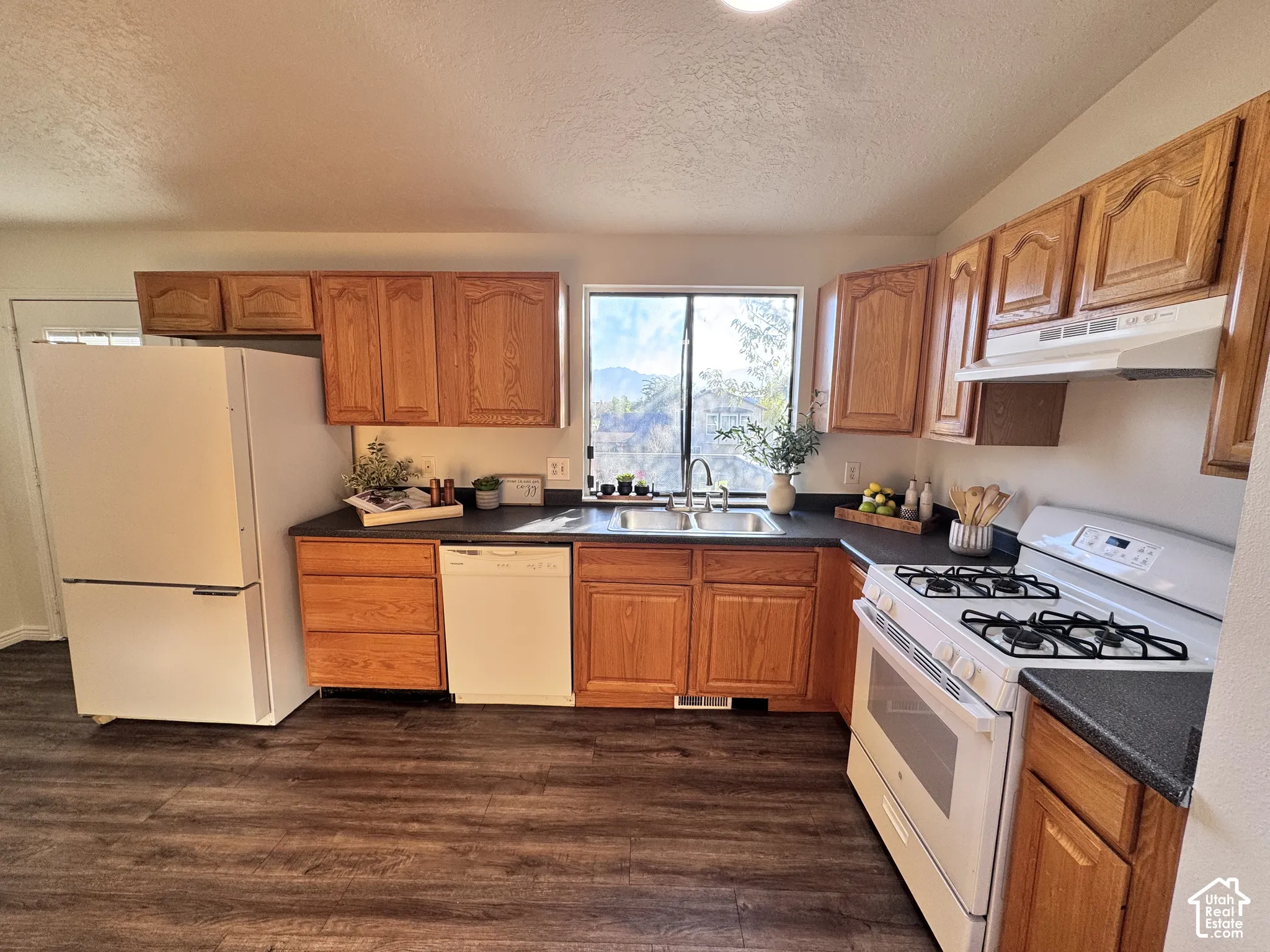 Kitchen featuring wood-finish cabinetry, dark countertops, a stainless steel sink, and wood-finish flooring
