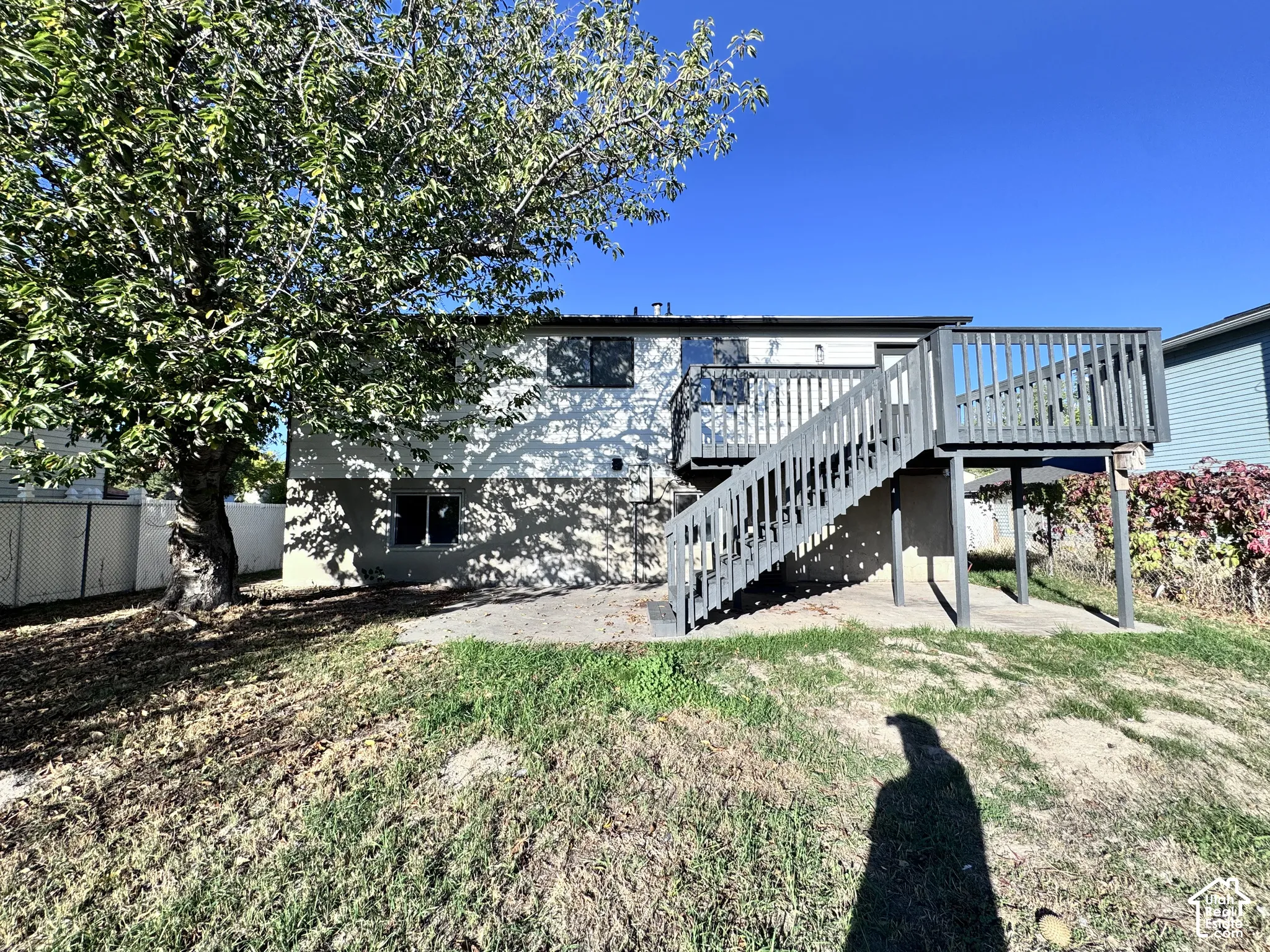 Exterior featuring a raised deck with stairs, a mature tree, and a sloped lawn